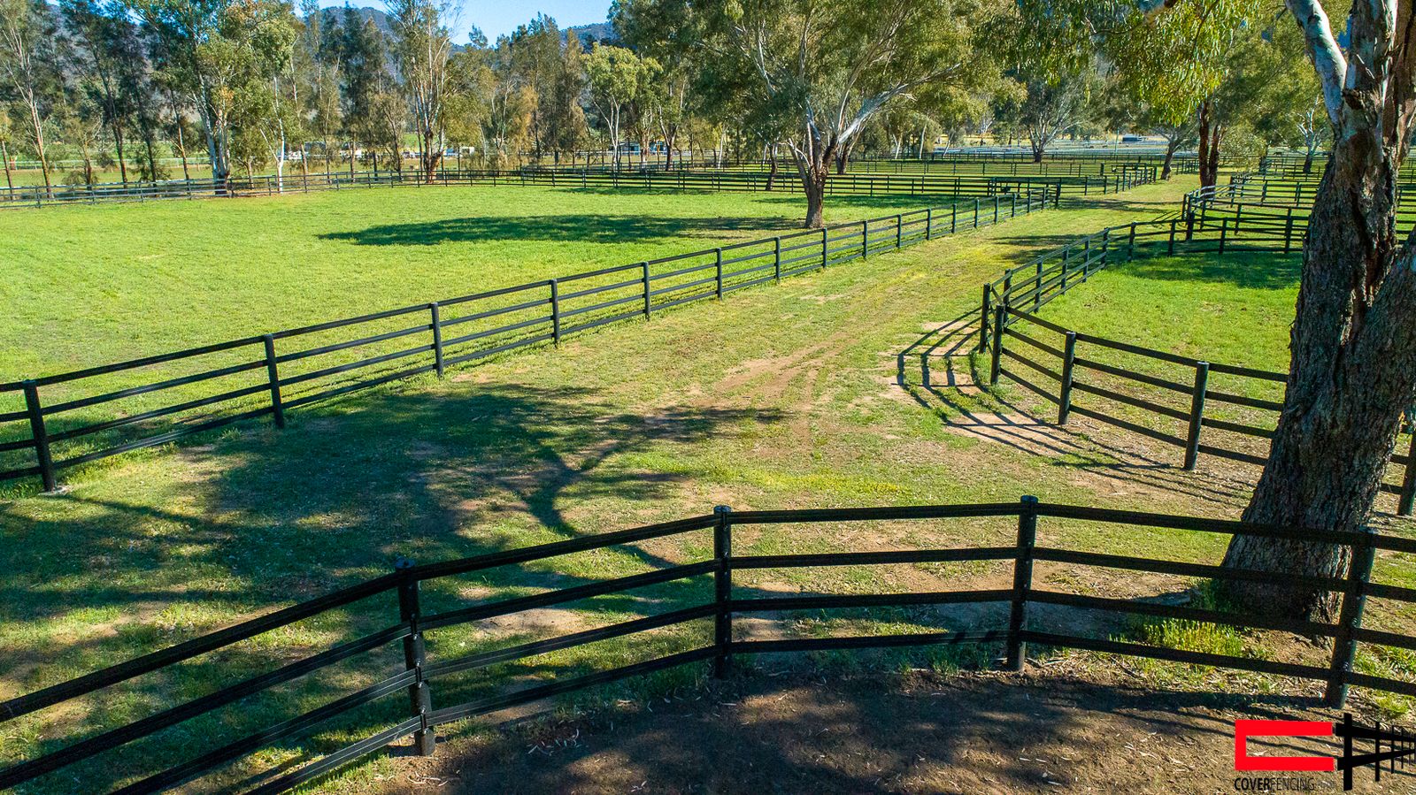 Curved post-and-rail fence line through a paddock, low angle, hills behind